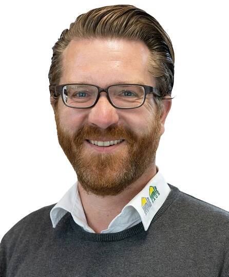 Porträt eines lächelnden Mannes mit Brille, der ein Hemd mit dem Logo von WOLF Haus trägt. Moderne Fertighauslösung in Wien.