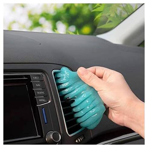 a model's hand using the blue cleaning putty to remove dirt from a car's dashboard air vent