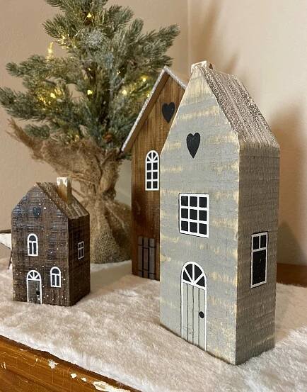 three wooden houses sitting on top of a table next to a small christmas tree with lights
