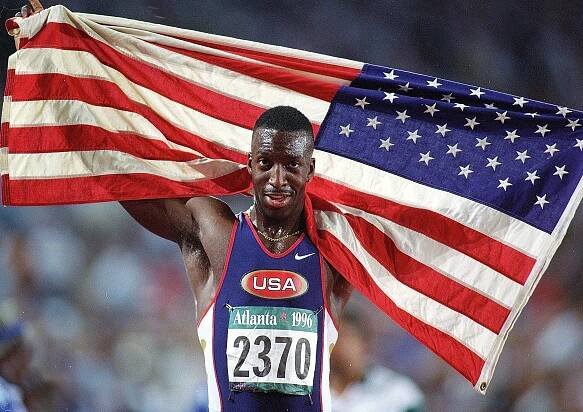 Michael Johnson, a US track and field athlete, carries the American flag after winning a gold medal.