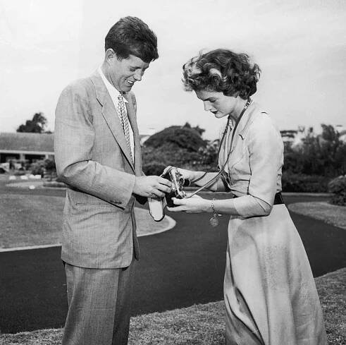 John F Kennedy (1917 - 1963) helping his wife, Jacqueline Bouvier Kennedy (1929 - 1994), adjust a camera in front of their home in Hyannis Port, Massachusetts