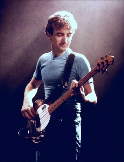 a young man playing an electric guitar in front of a dark background with spotlights