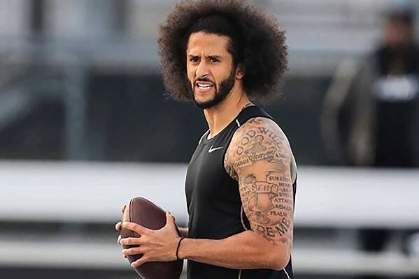 Colin Kaepernick holding a football and showing off tattoos on his upper arm on a field