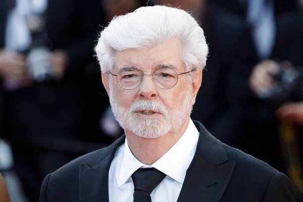 A man with white hair and a beard wearing a dark suit and tie.