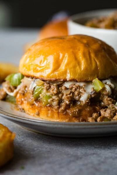 A photo of a philly cheesesteak sloppy joe on a toasted brioche bun on a white plate.