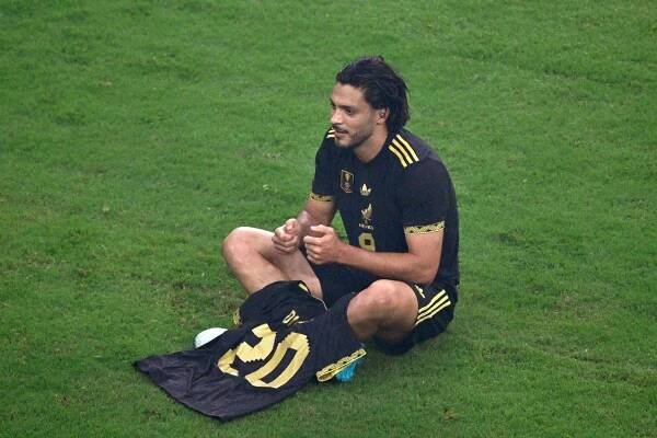 Raul Jimenez, wearing a Mexico soccer jersey, sits on the field holding a jersey with the number 21.