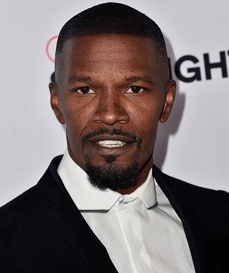 Jamie Foxx with short hair and a goatee while wearing a black blazer and white button-down