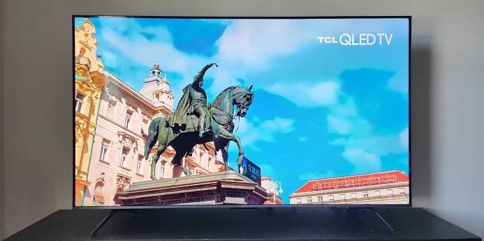 A TCL QM6K TV rests on a media console, and the screen shows an image of a statue of a man on a horse.