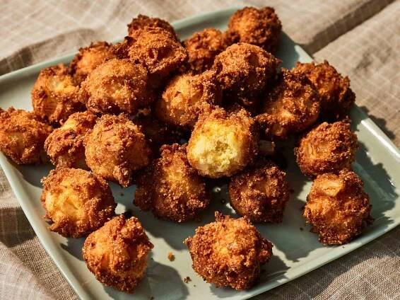 a plateful of golden-brown hush puppies with one broken into.