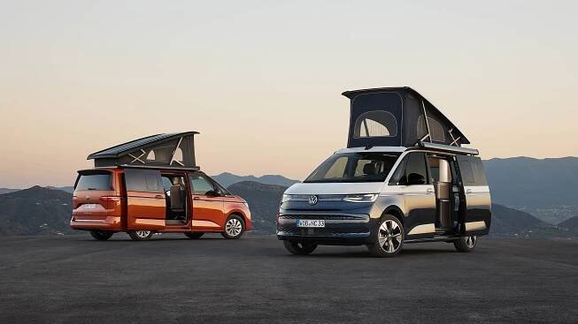 Zwei nebeneinanderstehende VW California mit aufgestelltem Hochstelldach und geöffneten Schiebetüren.