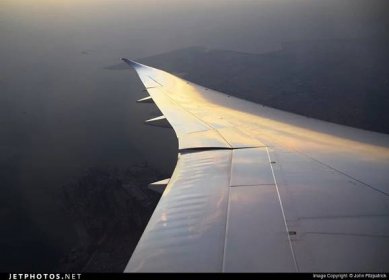 The view of an airplane wing with sky and ground behind