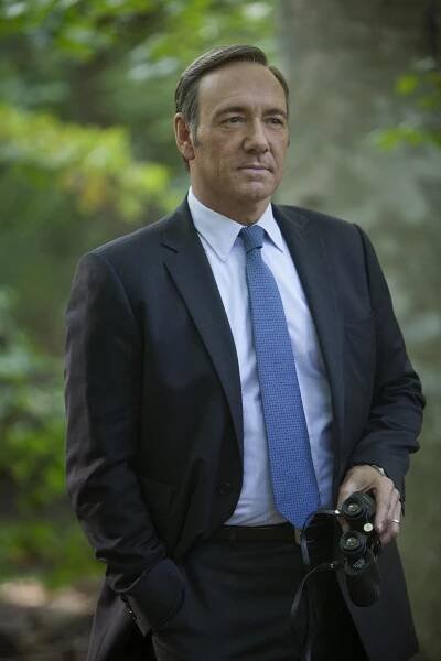 a man in a suit and tie standing next to a tree with a camera around his neck