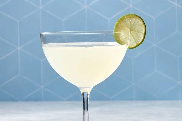 a classic daiquiri cocktail in a coupe glass with a lime garnish against a blue backdrop