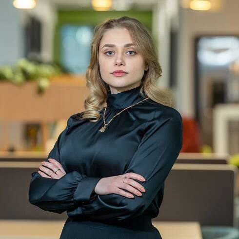 Professional woman in dark turtleneck blouse poses with crossed arms in modern office.
