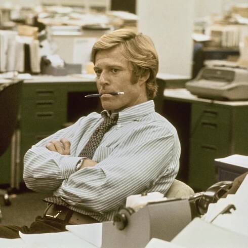 A man sits in an office with a pen in his mouth. 