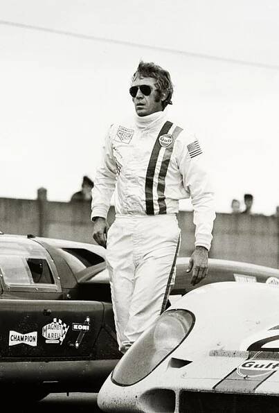 a black and white photo of a man standing next to a race car