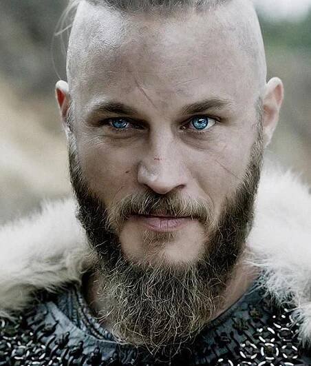 a bald man with blue eyes and a goatee is looking at the camera while wearing a fur collar