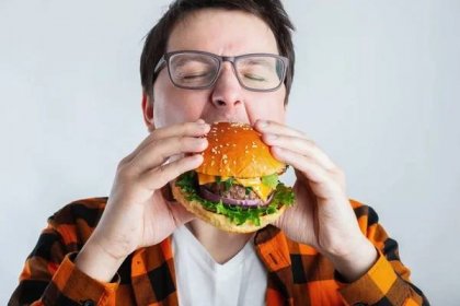 Mladý muž s brýlemi drží čerstvé Burger. Velký hlad student jí rychlého občerstvení. Teplé jídlo užitečné. Pojem obžerství a nezdravá strava. S kopií prostoru pro text. — Stock obrázek