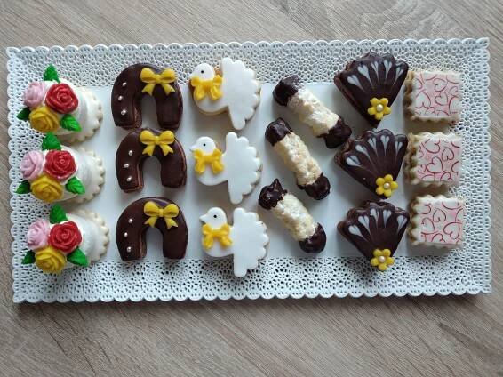 decorated cookies are arranged in the shape of letters on a white doily with pink and yellow flowers