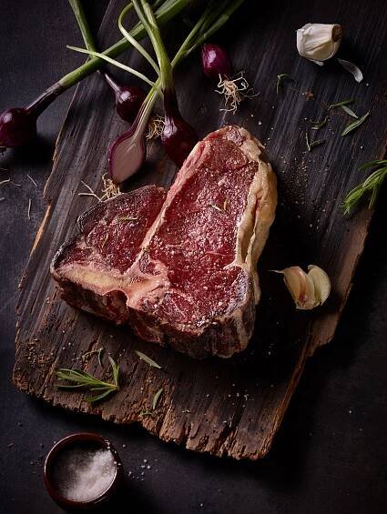 rare t-bone steak dry aged steak with salt garlic and spring onions on a wooden tablet dark food photography