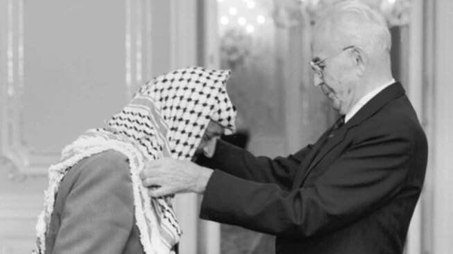 Návštěva Jásira Arafata v Praze, 18. října 1989. Do Československa tehdy přijel i Bassam Abu Sharif, podle amerického časopisu Time nejznámější tvář palestinského teroru. Prezident ČSSR Gustáv Husák (vpravo) předal na Pražském hradě předsedovi výkonného výboru OOP Jásiru Arafatovi Československý řád Bílého lva I. třídy.