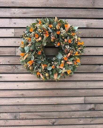 a wreath is hanging on the side of a wooden building with orange flowers and greenery