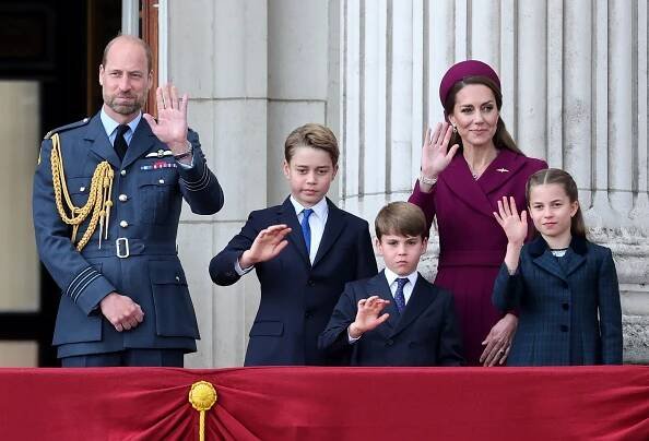 Prince William joins Catherine, Princess of Wales, and their children on the balcony during the VE Day 80th anniversary. William wears a formal Royal Air Force uniform while the entire family waves at the crowd.