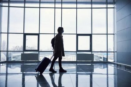 Stylový muž v lékařské masce nesoucí cestovní kufr na letišti — Stock fotografie