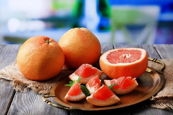Zralých grapefruitů na talíř, na dřevěný stůl, na světlé pozadí — Stock obrázek