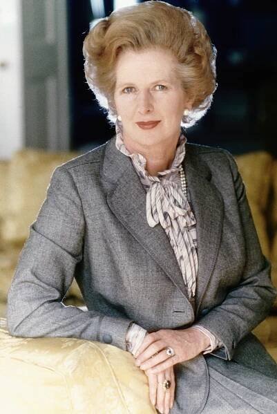 I don't know who this is, but the person is seated, wearing a tailored suit with a striped blouse and pearl necklace, posing confidently