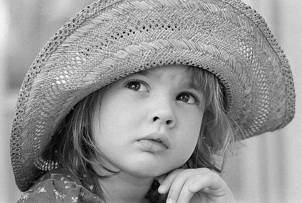 Child in a large straw hat gazes thoughtfully upwards, wearing a patterned shirt