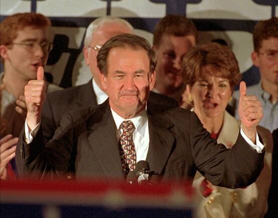 Pat Buchanan gives two thumbs up at a lectern. 
