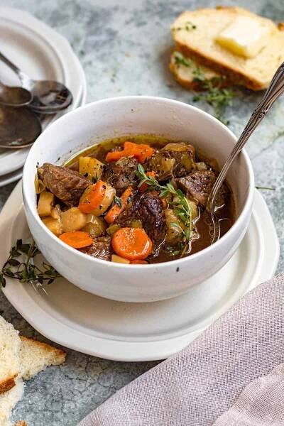 Bowl of Irish stew recipe with a spoon tucked in and a pat of butter on a piece of bread. 