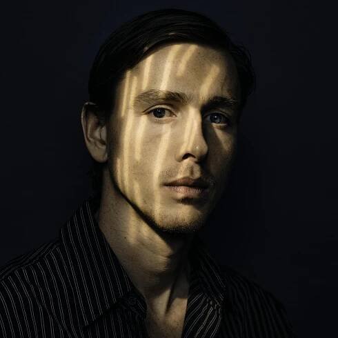 A portrait of Harris Dickinson dappled by shadows.