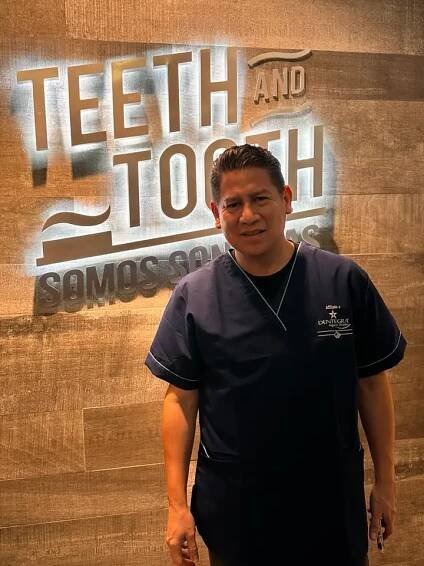 a dentist smiling with a bright sign in the background that says 'Teeth and tooth'