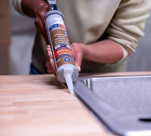 Someone applying silicone sealant to the outer edge of a sink.