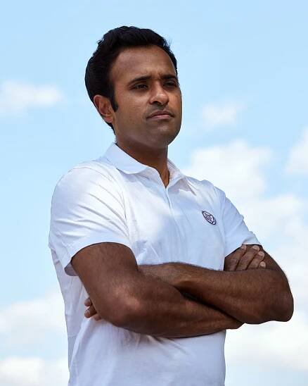 Vivek Ramaswamy standing with his arms crossed, with a cloudy blue sky in the background.