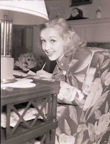 Betty Grable Smiling At The Camera While Seated And Writing In A Chair, 1939.