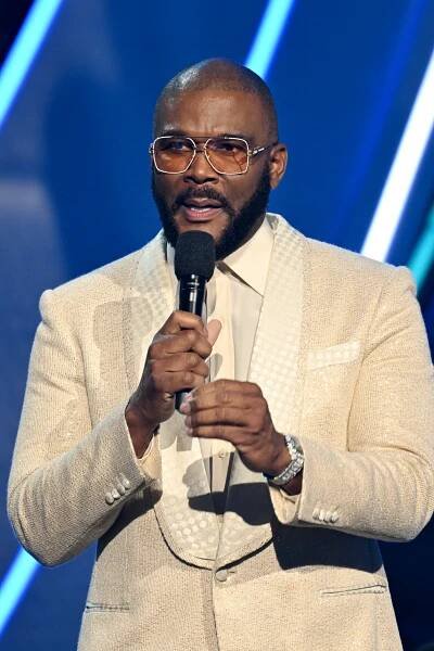 Tyler Perry in a white suit holding a microphone.