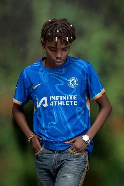 Free A young man poses confidently in a blue Chelsea FC football jersey with hands in pockets against a blurred natural backdrop. Stock Photo