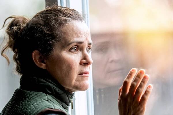 A pensive mature woman looks out a window.
