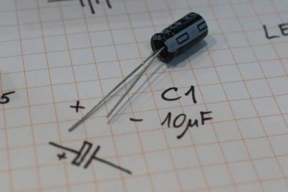 Elektrolytický kondenzátor C1 o hodnotě 10uF. Záporný vývod je většinou ten kratší a označený šedým pruhem na těle kondenzátoru.