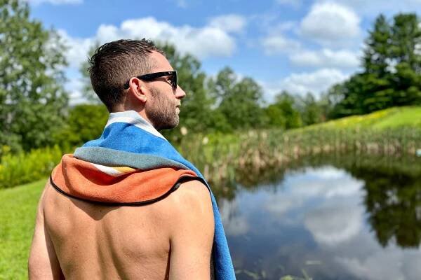 A person wearing the The Nomadix Original Towel next to a pond