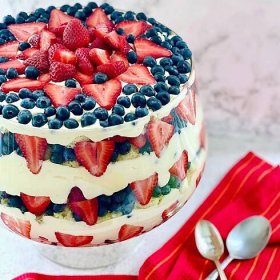 a combination of strawberries, blueberries and pudding layered with pound cake in a large glass punch bowl.