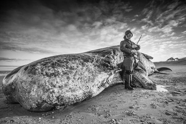 A member of the public poses in old fisherman's gear with a Sperm whale bull found stranded on the beach.A 40-foot-long Sperm whale bull was washed up on the beach at Old Hunstanton, in Norfolk, probably due to the fact that there are no squid to sustain this type of whale in the North sea. UK. 26th December 2011
