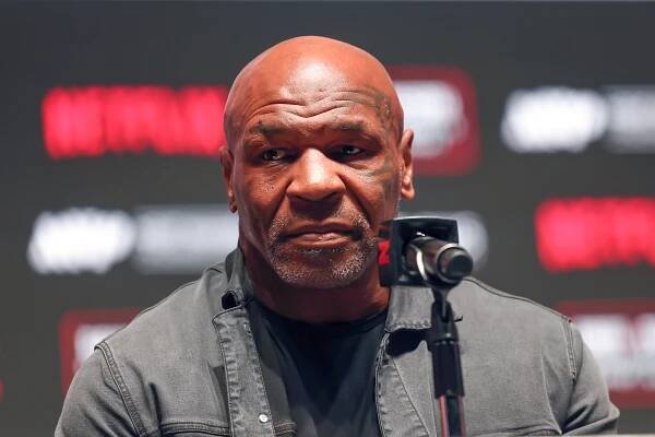 Mike Tyson, in a gray jacket, sits in front of a microphone.