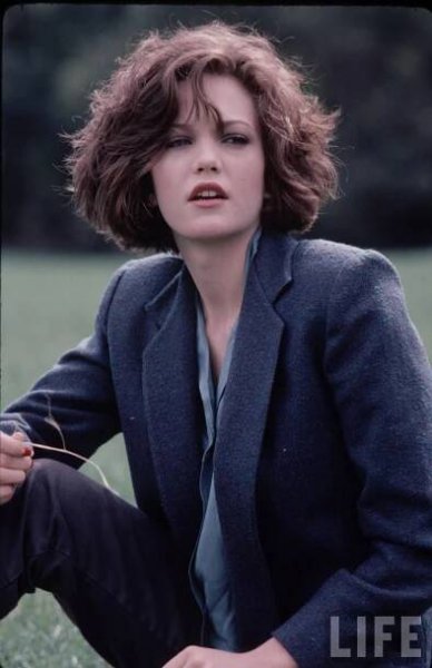 a woman sitting in the grass with her hands on her hips and looking off into the distance