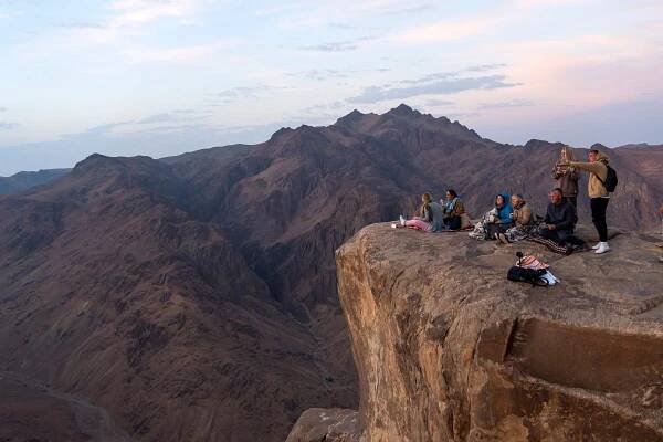Turisté sedí na okraji útesu a sledují východ slunce. Trekking na horu Mojžíš. Sinajský poloostrov Egypt. stock fotka