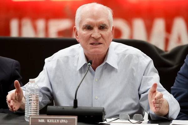 Representative Mike Kelly of Pennsylvania, wearing a striped button-down shirt, is seated and speaks into a microphone.