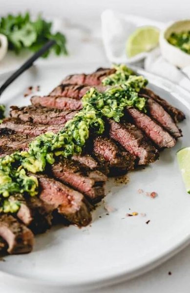 Closeup of sliced grilled flank steak with avocado chimichurri on top.